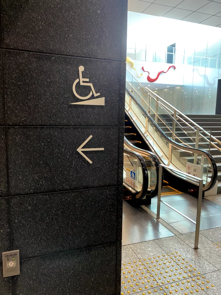 写真: 壁に車椅子マークが表示されており、その下側には進む方向を伝える矢印が表示されている