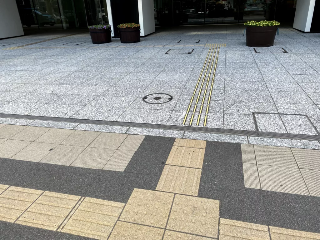 写真: 歩道の点字ブロックと創世スクエアの敷地の点字ブロックが繋がるように設置されている。